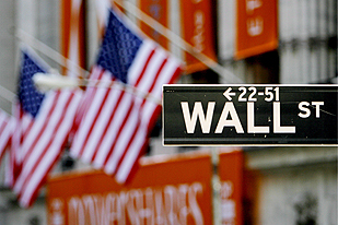 A close-up of the sign for Wall Street is seen with the US flags on the New York Stock Exchange in the background in New York City, the US.
