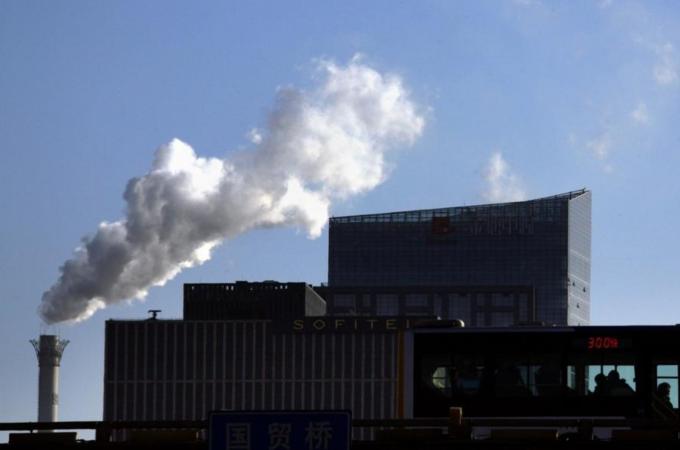 Passengers on a bus can be seen in front of a chimney for a coal-burning heating system as it billows smoke in central Beijing