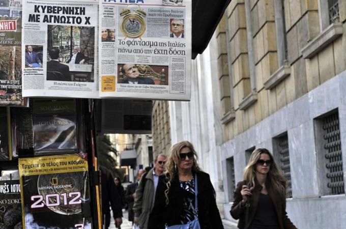 Women walk by Greek newspapers displayed