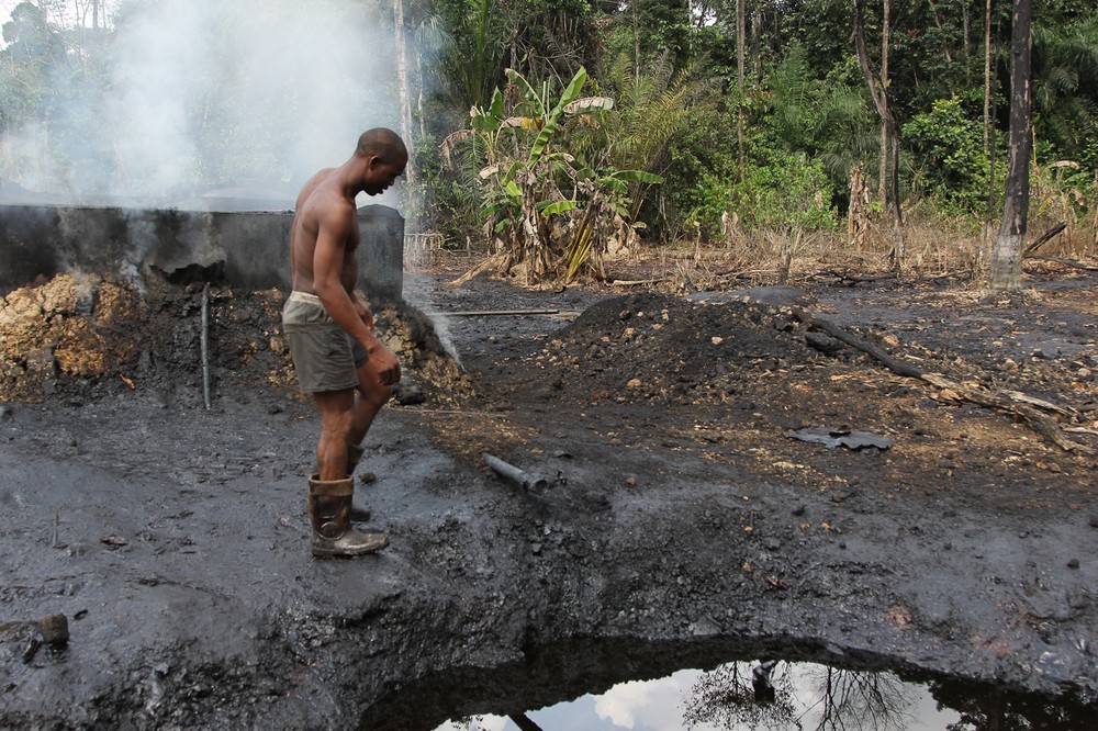 A worker at an illegal refinery camp inspects refinery equipment  
as smoke emerges from behind drums, near the Nun River in Nigeria(***)s oil 
state of Bayelsa.