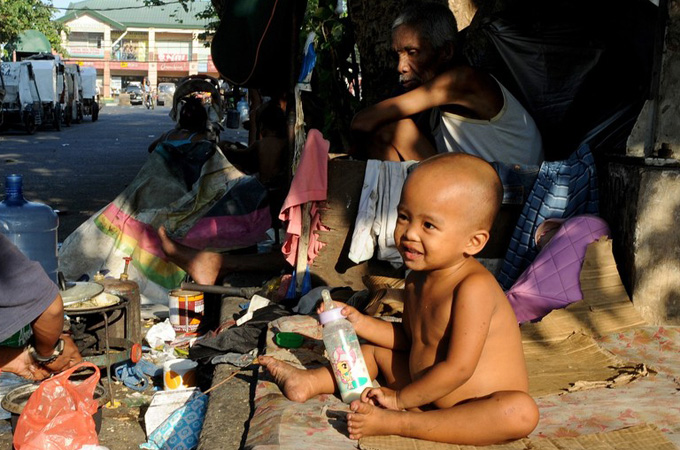 A Philippine street child holds her bottle as her grandparents look on behind in Manila [AFP]