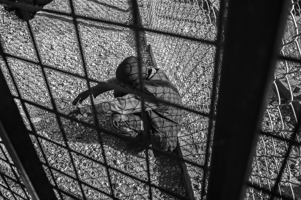 A young boy sits against a gate in the reception area waiting to be registered as a refugee at Za(***)atari refugee camp.