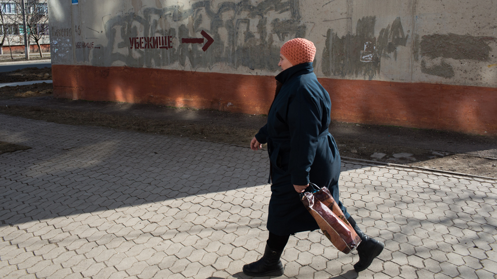 
A woman passes a sign for a bomb shelter in Vostochniy, a neighbourhood in Mariupol near the front line [John Wendle/Al Jazeera]

