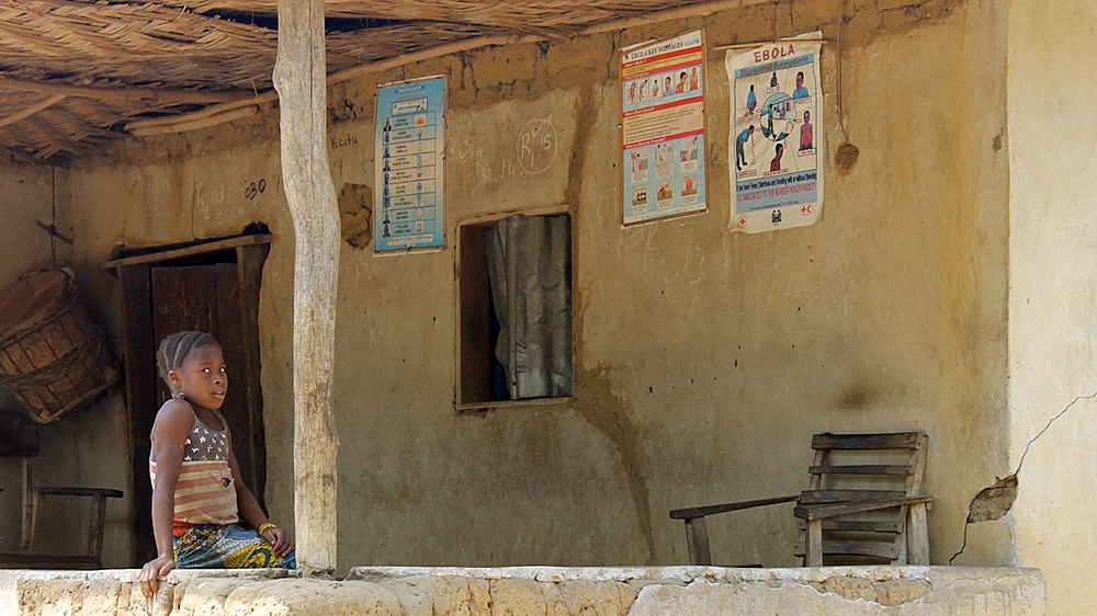 A girl sits under an Ebola information poster [Dariusz Dziewanski/Al Jazeera] 