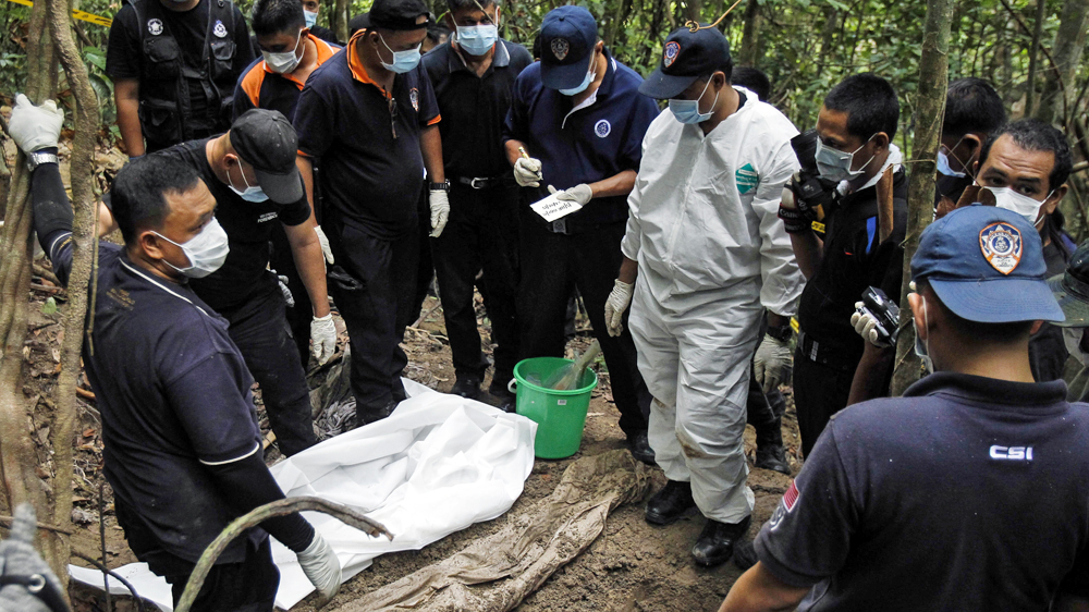 Malaysian police forensic team members inspect a freshly exhumed human body