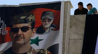 Syrians look down at a poster of Assad and his late father in Damascus [AFP]