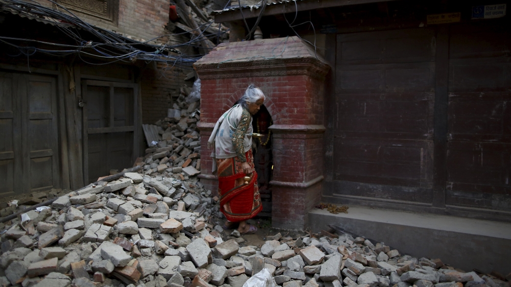 A woman walks on top of debris of a collapsed house as she returns after offering daily prayers at a temple, a month after the earthquake in Kathmandu, Nepal [REUTERS]