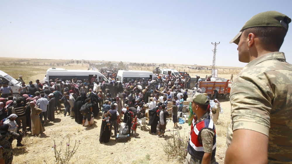 Turkish soldiers stand guard as Syrian refugees wait for transportation after crossing into Turkey from the Syrian town of Tal Abyad, near Akcakale in Sanliurfa province, Turkey