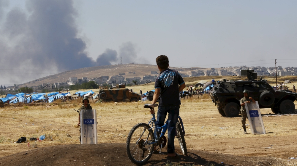 Turkish Kurdish boy stands near the Mursitpinar border gate in Suruc in Sanliurfa province, Turkey, as smoke rises in the Syrian town of Kobani in the background