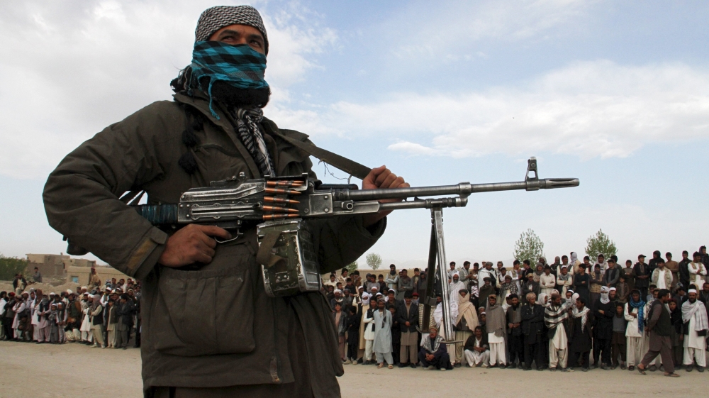 A member of the Taliban insurgent and other people stand at the site during the execution of three men in Ghazni Province