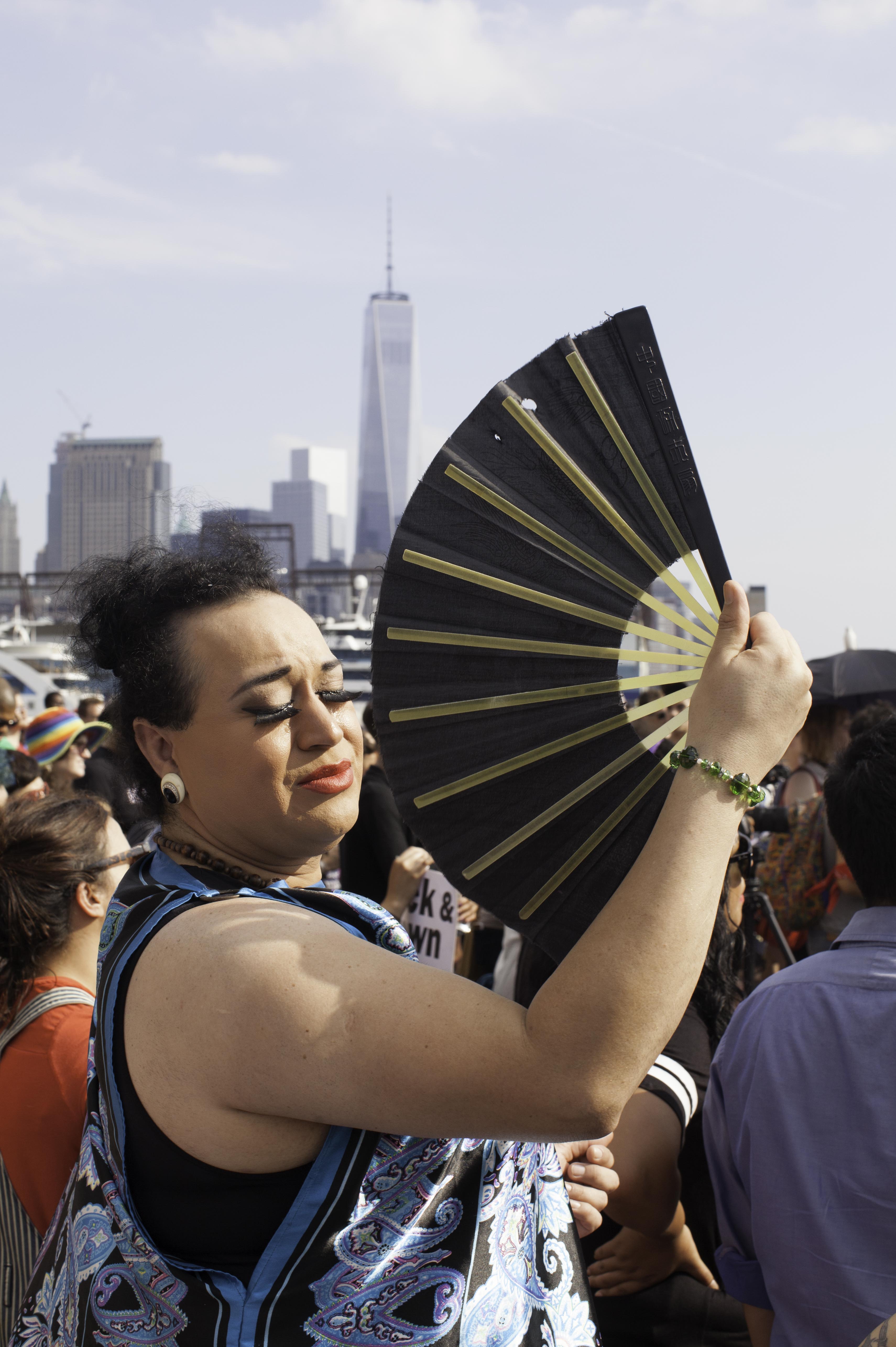 A participant in the Trans Day of Action cools off with an oversized fan. The newly built One World Trade Center can be seen in the background [Joey Prince] [Daylife]