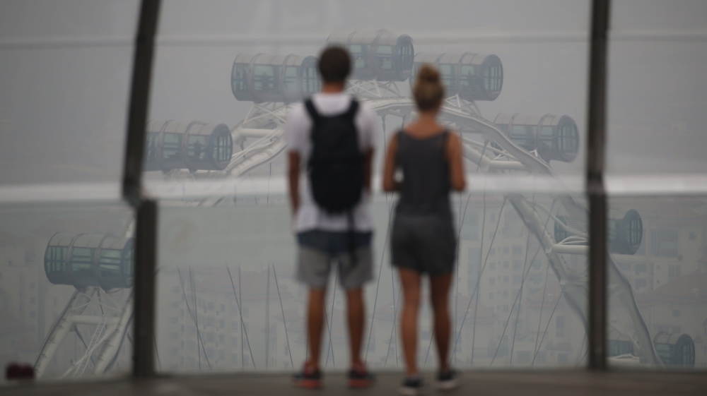 Tourists look at the Singapore Flyer observatory wheel shrouded by haze in Singapore