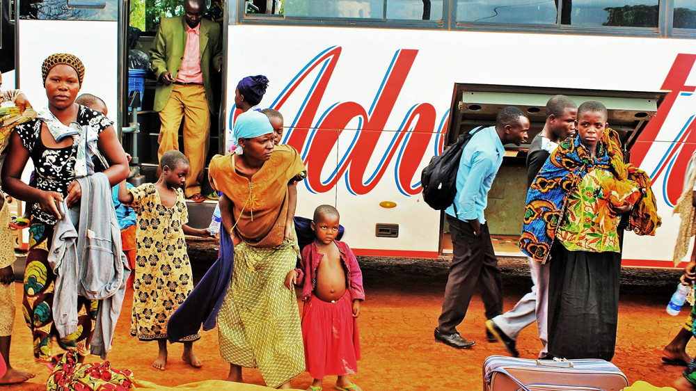 New arrivals from Burundi step off the bus, having been collected by humanitarian agencies from the border [Tendai Marima/Al Jazeera]