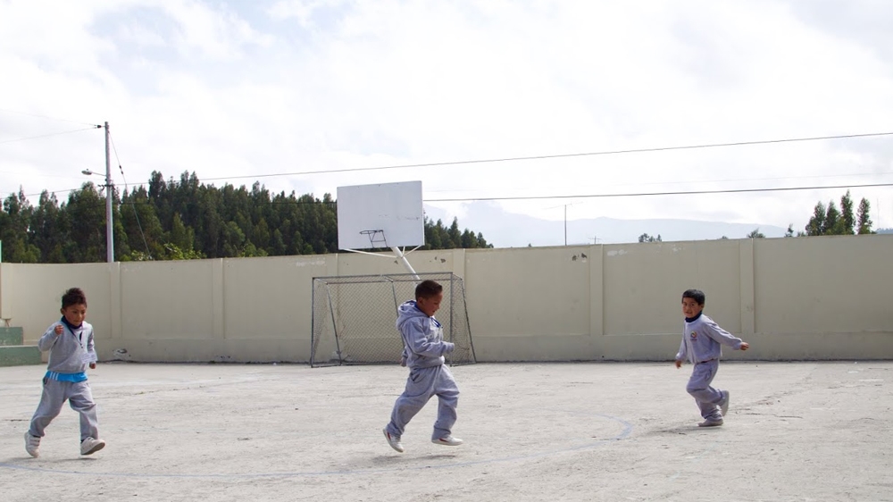 Children play in their school compound overlooking Cotopaxi in the distance [Priyanka Gupta/Al Jazeera]