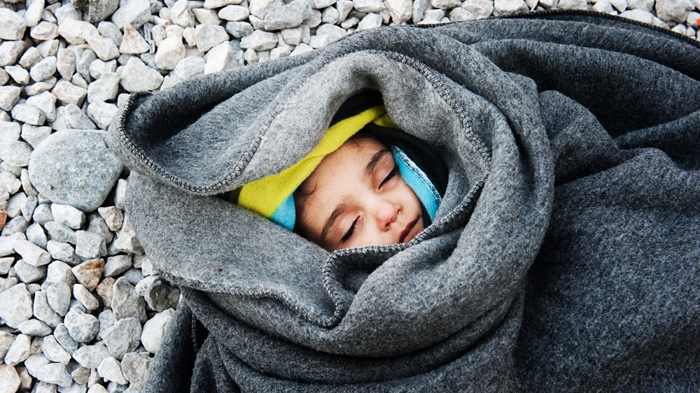 A child is wrapped in blankets on the ground. But they can do little to keep out the bitter cold [Mona van den Berg/Al Jazeera]