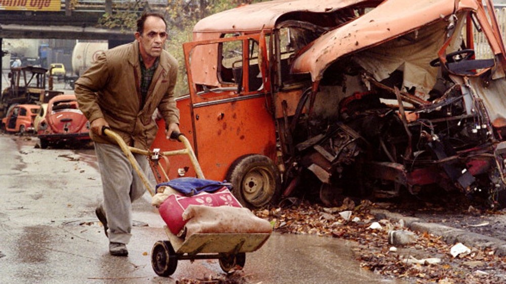 A Bosnian man pushing a cart rushes for cover while crossing a street exposed to snipers' fire on October 10, 1992, in Sarajevo [Patrick Baz/AFP/Getty Images]