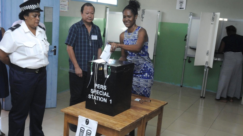 A police officer and an election official watch as a voter cast her ballot in the presidential polls in Victoria, Seychelles