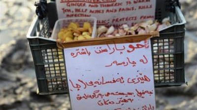 A volunteer hands out ginger, turmeric and garlic to camp residents, to help fight infection [Lydia Noon/Al Jazeera]