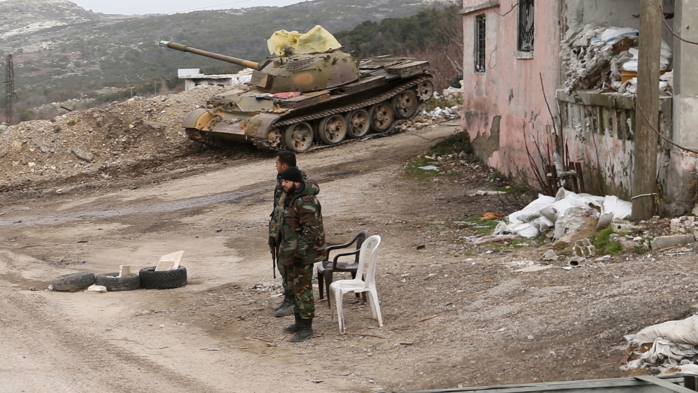 Syrian troops stand with a destroyed tank in the back