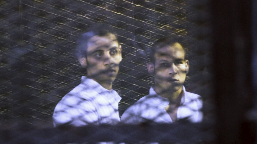 Defendants react as they are seen behind bars during their hearing at a court in Cairo