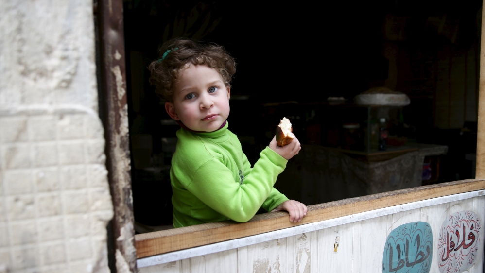 A child eats bread as she stands in front of a shop in the rebel held Qaboun neighborhood of Damascus, Syria [Reuters]