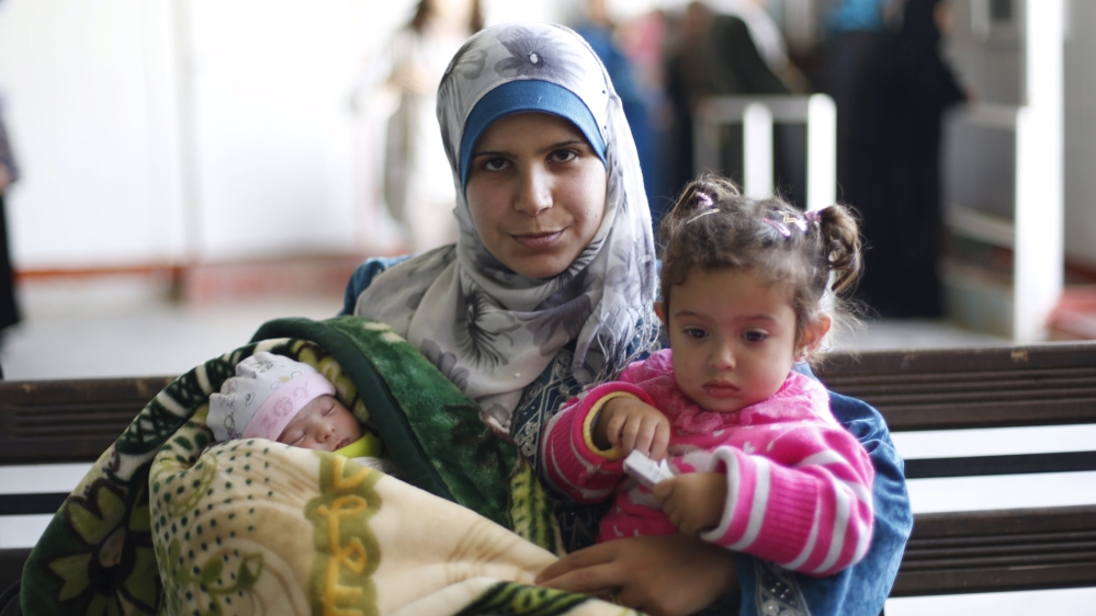 A Syrian refugee carries her daughters at Al Zaatari refugee camp