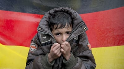A child tries to warm his hands, backdropped by Germany''s flag