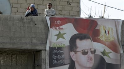 Residents stand near a picture of Syria's president Bashar al-Assad in Wafideen Camp, in Damascus [Reuters]