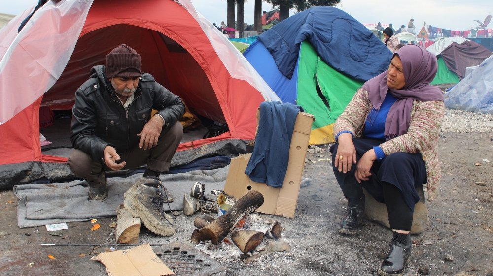 An elderly couple use a tin can to warm up water for tea [John Psaropoulos/Al Jazeera]