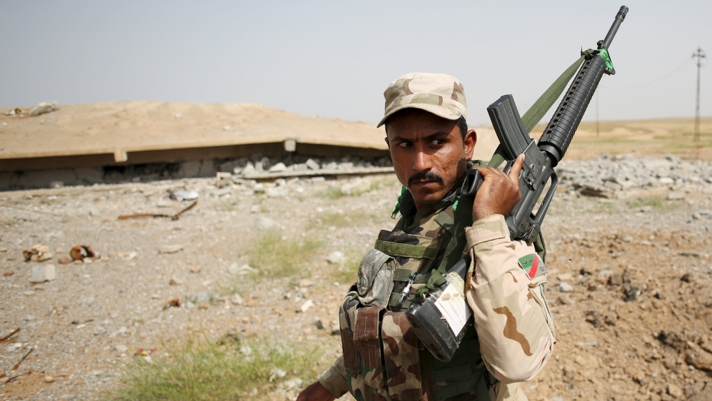 An Iraqi soldier holds up his rifle in front of a building destroyed by an airstrike in a village south of Mosul, Iraq [REUTERS]