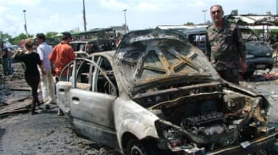 An officer standing next to damaged cars at the site of car bombing in a bus station in the Jableh city, Latakia province, Syria [EPA]
