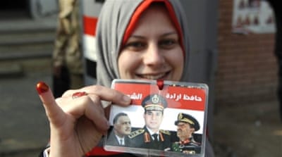 An Egyptian woman holds a card bearing portraits of Gamal Abdel Nasser, Anwar Sadat and Abdel Fattah el-Sisi ([AFP] 