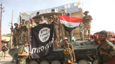 Shia fighters and Iraqi security forces hold an ISIL flag, which they pulled down after clashes with ISIL north of Fallujah, Iraq [Reuters]