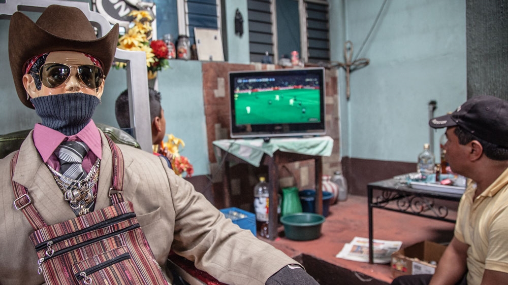 San Simon/Maximon sits behind the shrine along with his attendants. Although there are many variations, he is typically portrayed in a cowboy hat and sunglasses [  Gabriela Campos/Al Jazeera]  