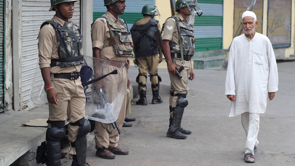 A Kashmiri man walks past security forces in central Srinagar, as the curfew is eased [Aarabu Ahmad Sultan/Al Jazeera]