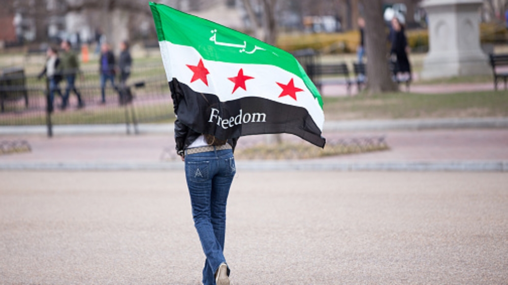 A woman carries a Syrian freedom flag in a park across the street from the White House in Washington DC [Getty]