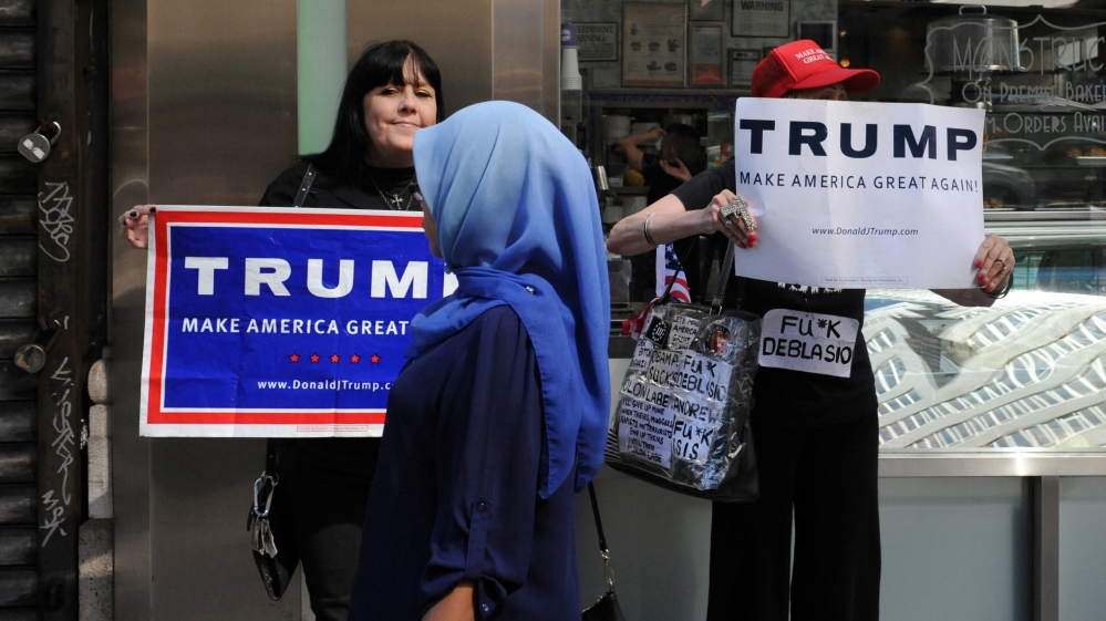 A woman wearing a Muslim headscarf walks past people holding U.S. Republican presidential nominee Donald Trump signs before the annual Muslim Day Parade in the Manhattan borough of New York City