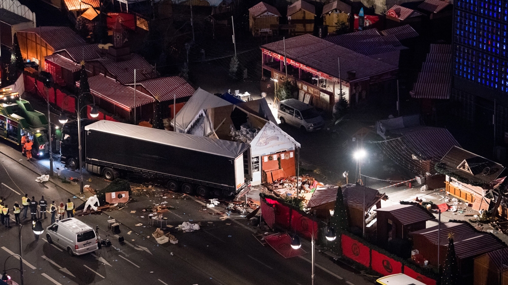 Workers secure a truck to a recovery vehicle, left, at the scene where the truck crashed into a Christmas market near the Kaiser Wilhelm Memorial Church in Berlin [Bernd Von Jutrczenka/EPA] 
