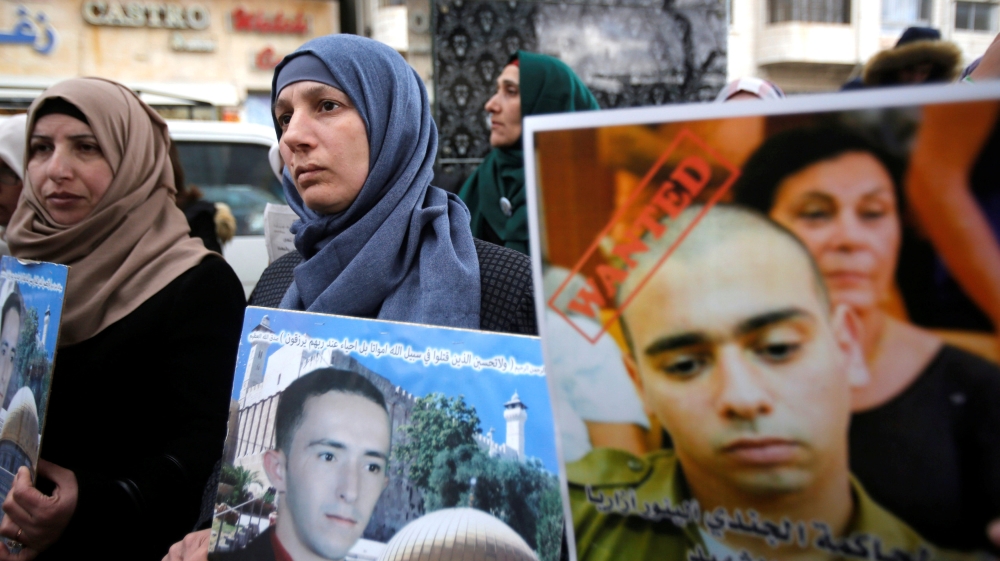 The mother of Palestinian assailant Abdel Fattah al-Sharif holds his poster as another woman holds a poster of Israeli soldier Elor Azaria during a protest in the West Bank city of Hebron