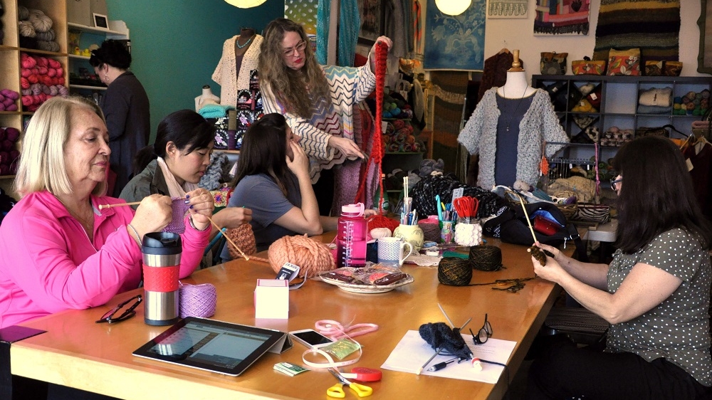 Kat Coyle, standing, designed the first hat pattern [Melissa Chan/Al Jazeera]
