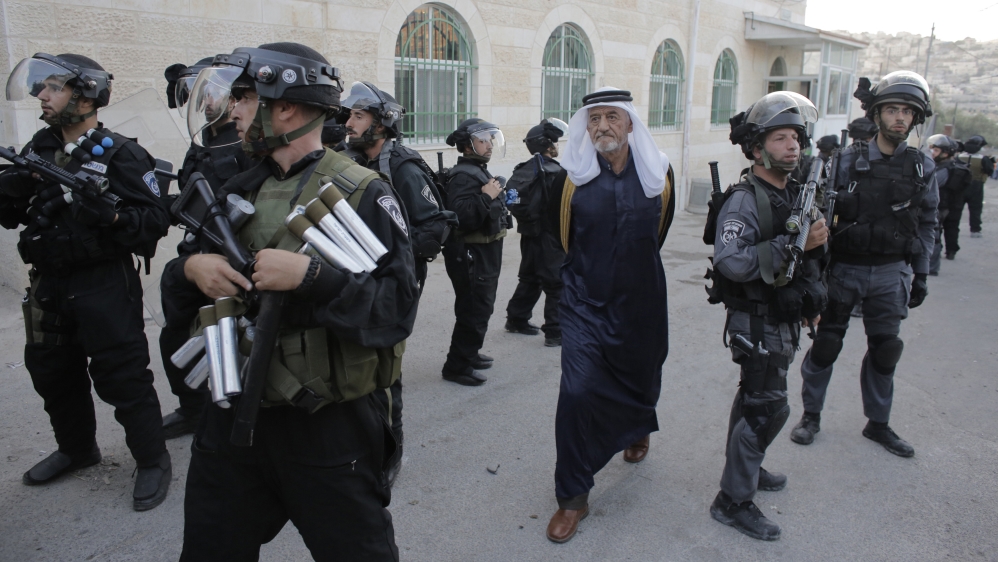 A man walks past Israeli police officers in Jabal Mukaber, near the home of a Palestinian suspected of an attack [Ammar Awad  /Reuters]