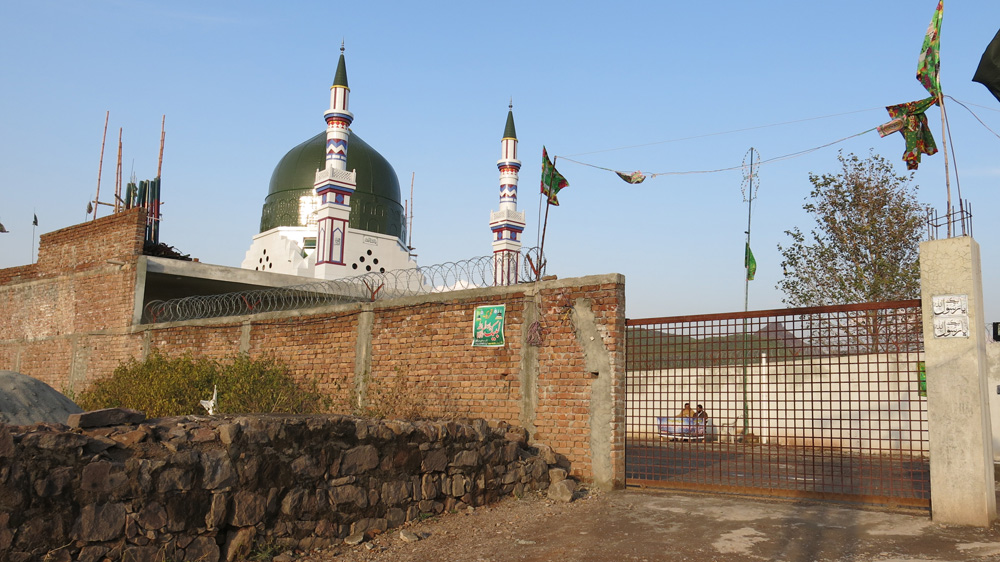 A bookseller sells portraits of Mumtaz Qadri and books written in his honour just outside the shrine [Asad Hashim/Al Jazeera]
