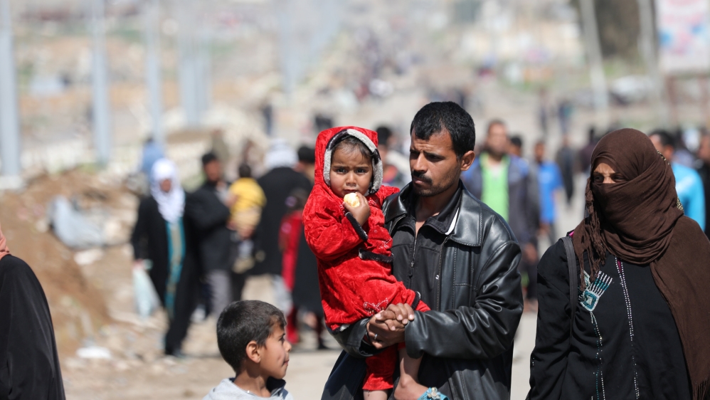 An Iraqi man carries a girl on his arms as he walks along a street after fleeing his house in the city of Mosul