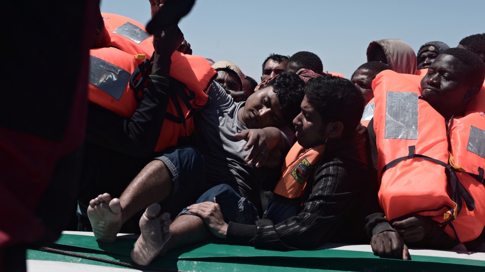 Migrants in an overcrowded plastic raft reach out for life jackets during a search and rescue operation by rescue ship Aquarius, operated by SOS Mediterranean and Doctors without Borders