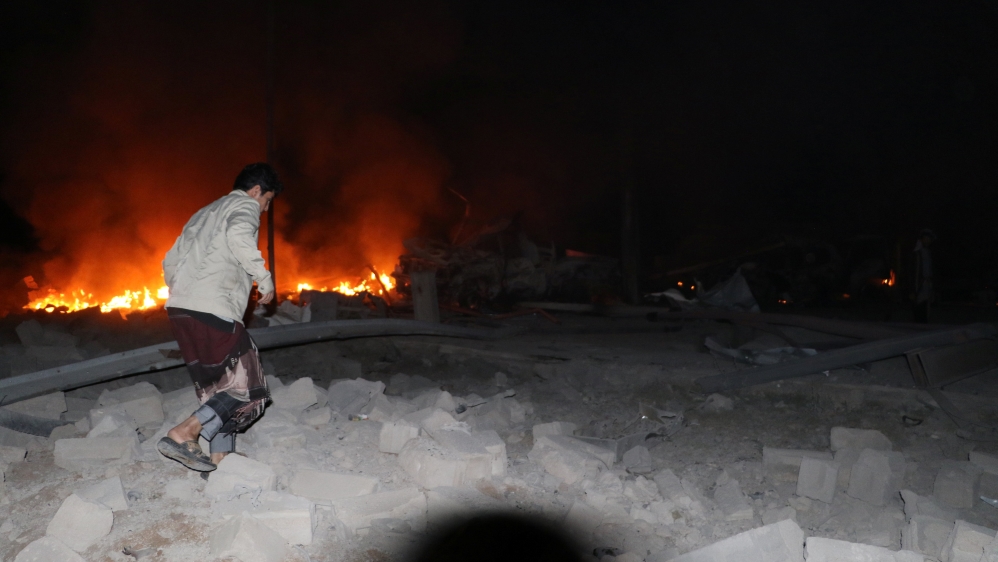 A man walks in front of a fire that broke out at the site of a Saudi-led air strike which hit a car repair workshop in the northwestern city of Saada