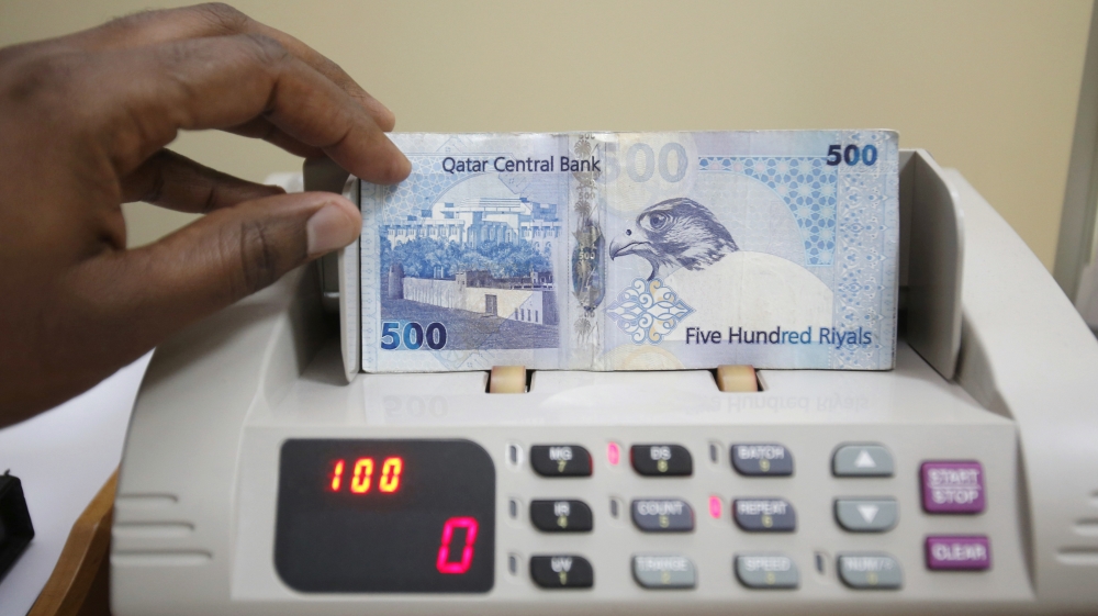 A cashier counts Qatari riyal notes at a money changer in Doha