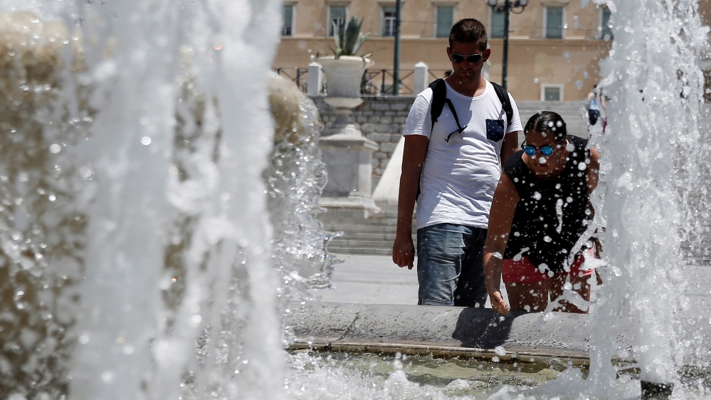 People cool off in a fountain of water during a hot Summer day in Athens