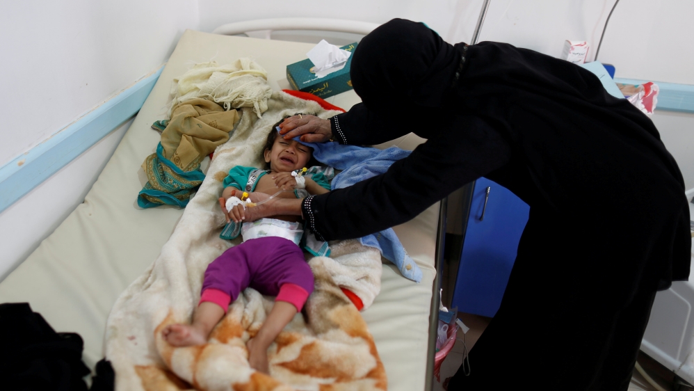 Woman helps her son as he lies on a bed at a cholera treatment center in Sanaa, Yemen