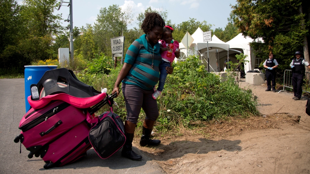 A mother and her daughter are watched by RCMP officers as they prepare to cross the U.S.-Canada border from Champlain in New York