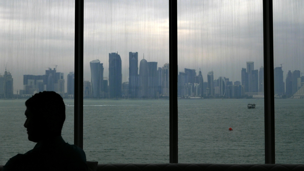 A man sits inside the Islamic art museum of Doha as the city''s skyline is seen in the background in Doha